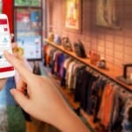 Een hand die een smartphone gebruikt om door de WooCommerce-winkel in een kledingwinkel te bladeren.