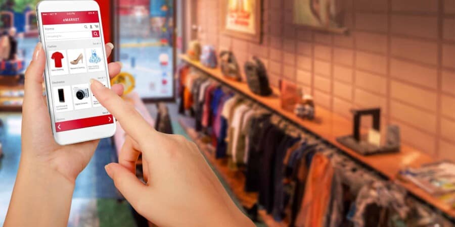 Een hand die een smartphone gebruikt om door de WooCommerce-winkel in een kledingwinkel te bladeren.
